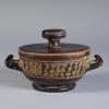 Photograph of a lidded lekanis, with lid in place, from the side against a neutral gray background.