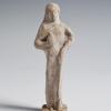Photograph of terracotta female figurine, frontal, against neutral gray background.