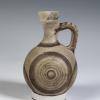 Photograph of a small, rounded jug, tan with brown decoration, against a neutral gray background.