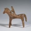 Photograph of horse and rider figurine, from the side with horse and rider facing toward viewer's left, against neutral gray background.