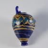 Photograph of a broken multi-colored glass vase with an ovoid body that tapers to a narrow, flat base. Neck and most of handle broken. From the side against a neutral gray background.
