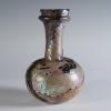 Photograph of a dark glass vessel with a globular body and somewhat tall neck that tapers out at the top, from the side against a neutral gray background.