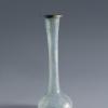 Photograph of a clear glass vessel with a squat globular body and a tall, narrow neck that flares toward the top to a rounded mouth, from the side against a neutral gray background.