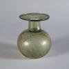 Photograph of a clear glass vessel with a round body and a relatively short neck that tapers into a horizontal, disk-shaped mouth, from the side against a neutral gray background.