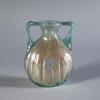 Photograph of a clear glass jar with a rounded body, two handles that connect the shoulders to the mouth, from the side against a neutral gray background.