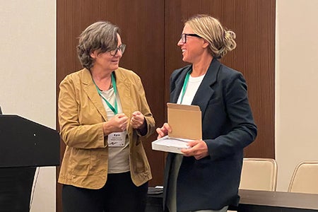 Ashley Carter accepts her best paper award from a woman onstage at the conference.