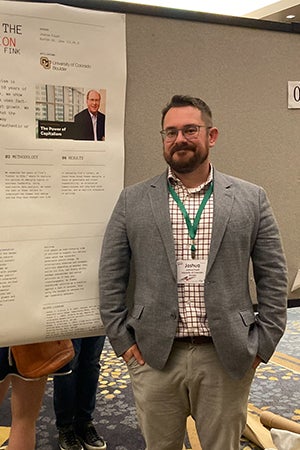 Josh Foust stands in front of a poster demonstrating his research work at the conference.