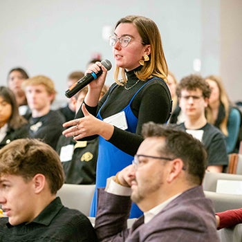 A female student stands to ask a question during a panel discussion.