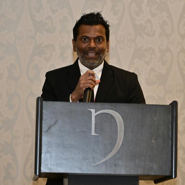 Harsha accepts his award at a podium.