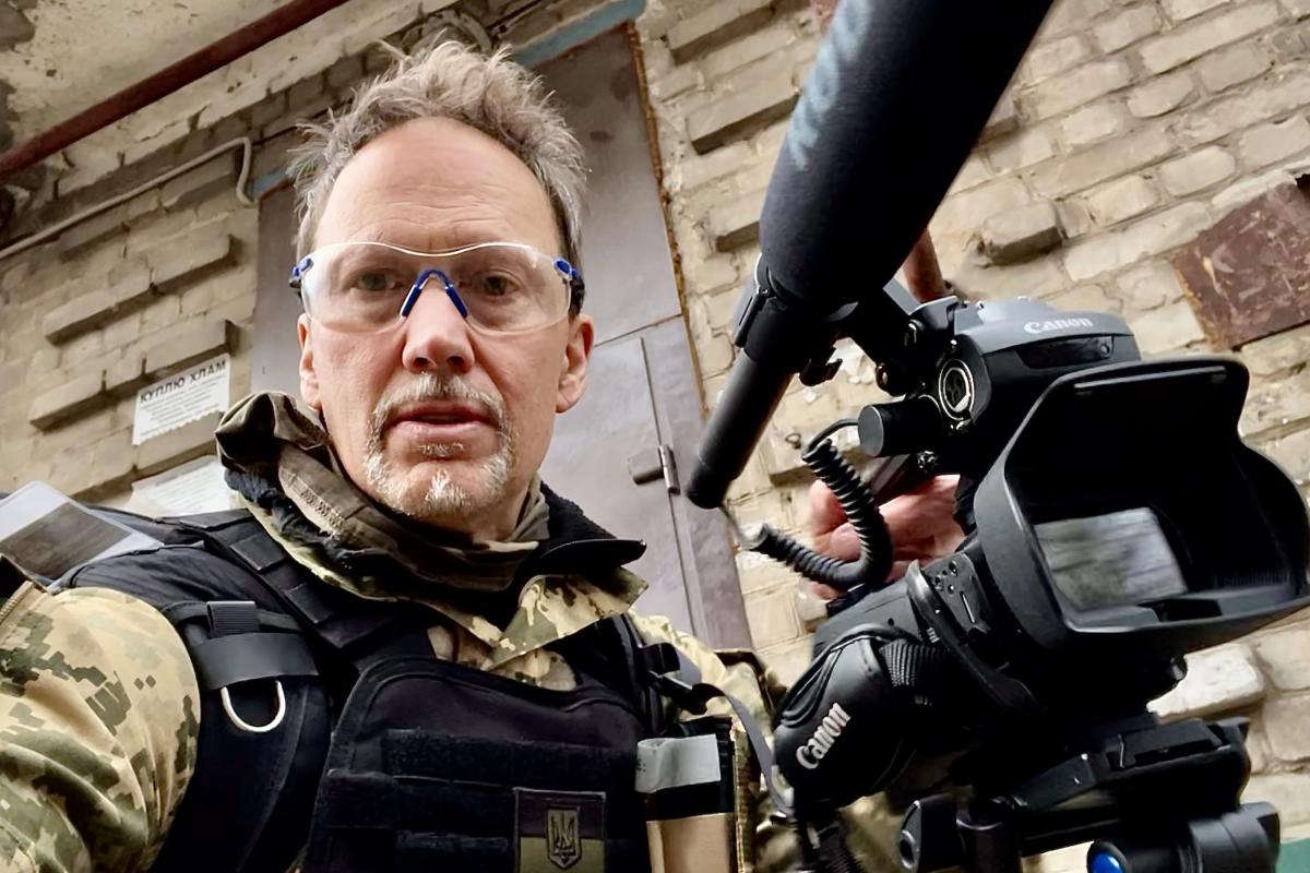 Jordan Campbell holding his camera and wearing combat fatigues in Ukraine.