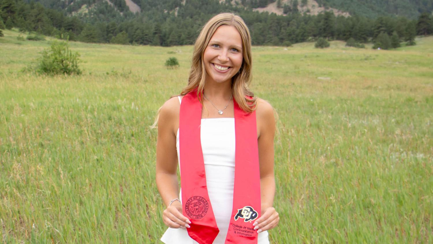 Henley Beisert stands at the Colorado Chautauqua wearing a white dress and red CMCI graduation sash.