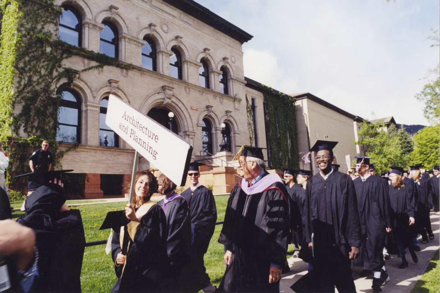 Peggy walking with the Architecture and Planning sign at graduation