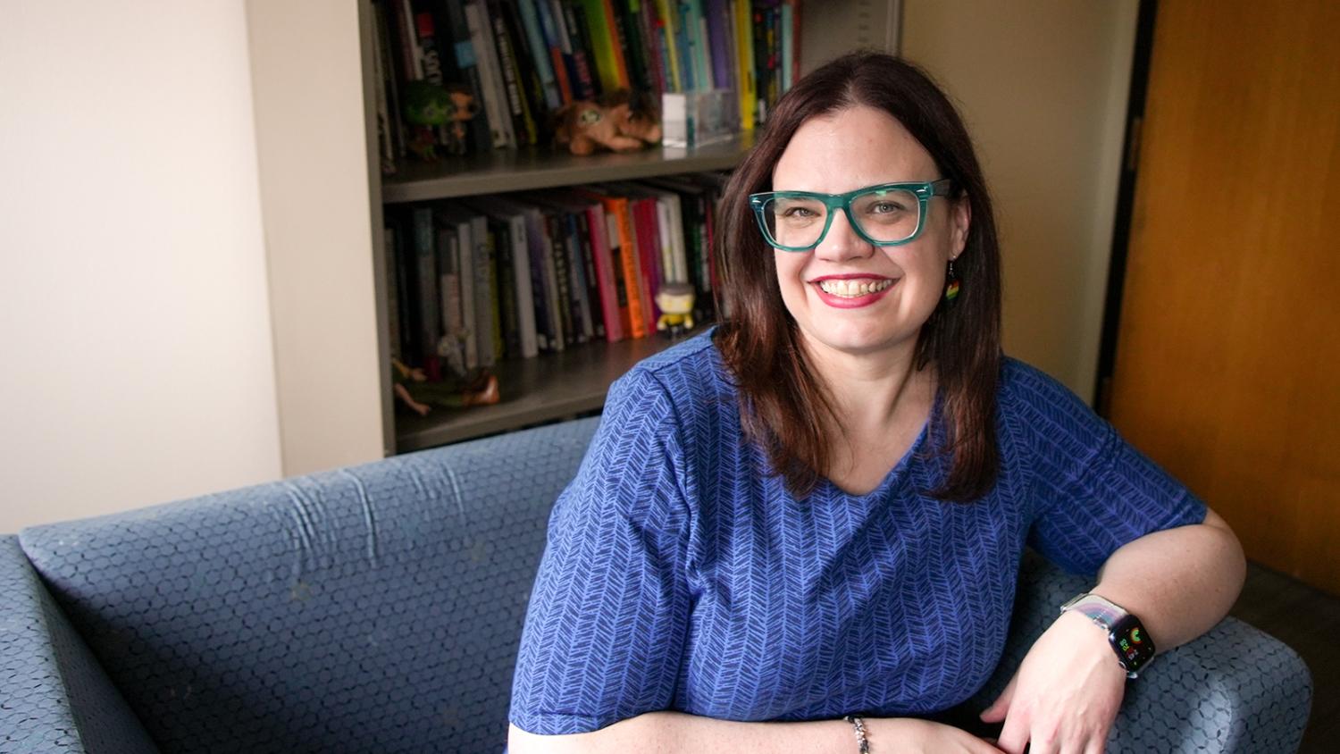 A female professor sits in her office. A bookshelf with books and personal mementoes is in the background.