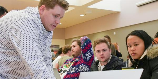 A senior shows his work on a laptop to two other students.