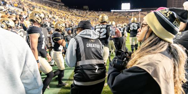 A group of students work the sidelines documenting media during a football game.