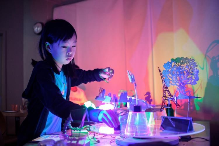 A girl works at a table of objects lit with lights.