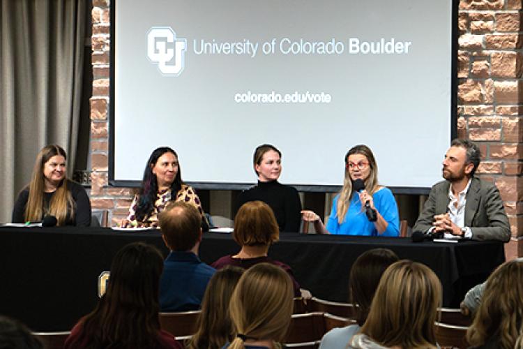 Four panelists listen as a woman speaks into a microphone.