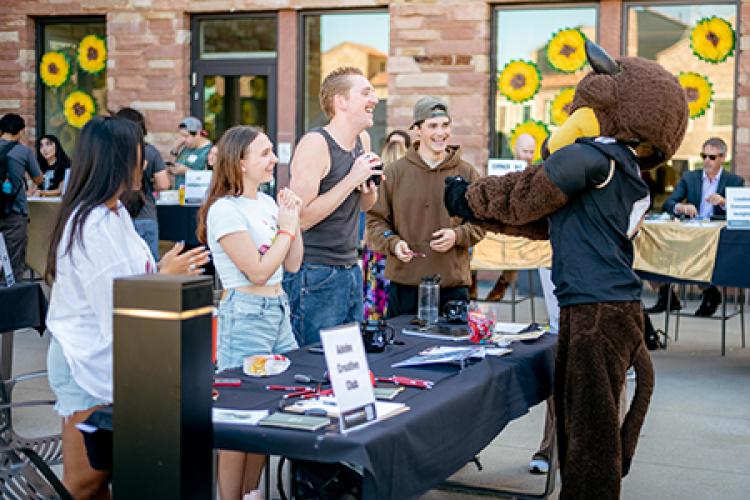 Chip, the CU mascot, takes selfies with students at a table.