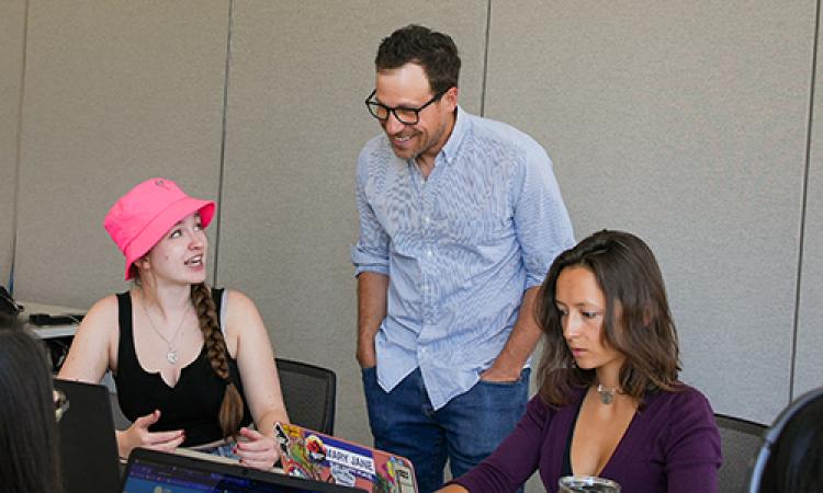 Pat Ferrucci talks to two students using computers in a CMCI classroom.