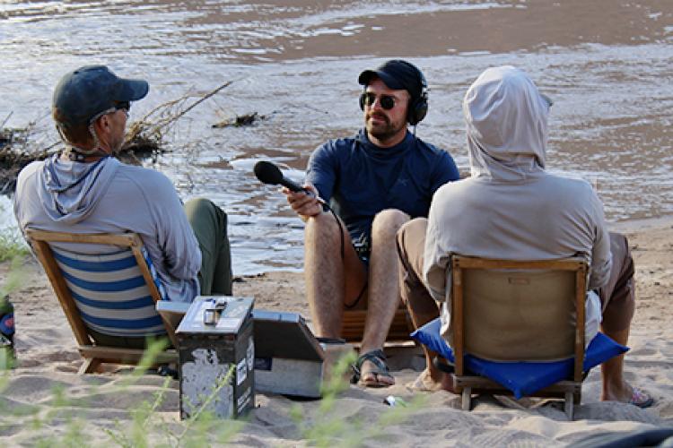 Luke Runyon records an interview with two men along the shore of the Colorado River.
