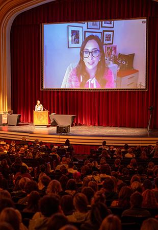 A speaker is projected on a screen in a packed auditorium as she answers a question.