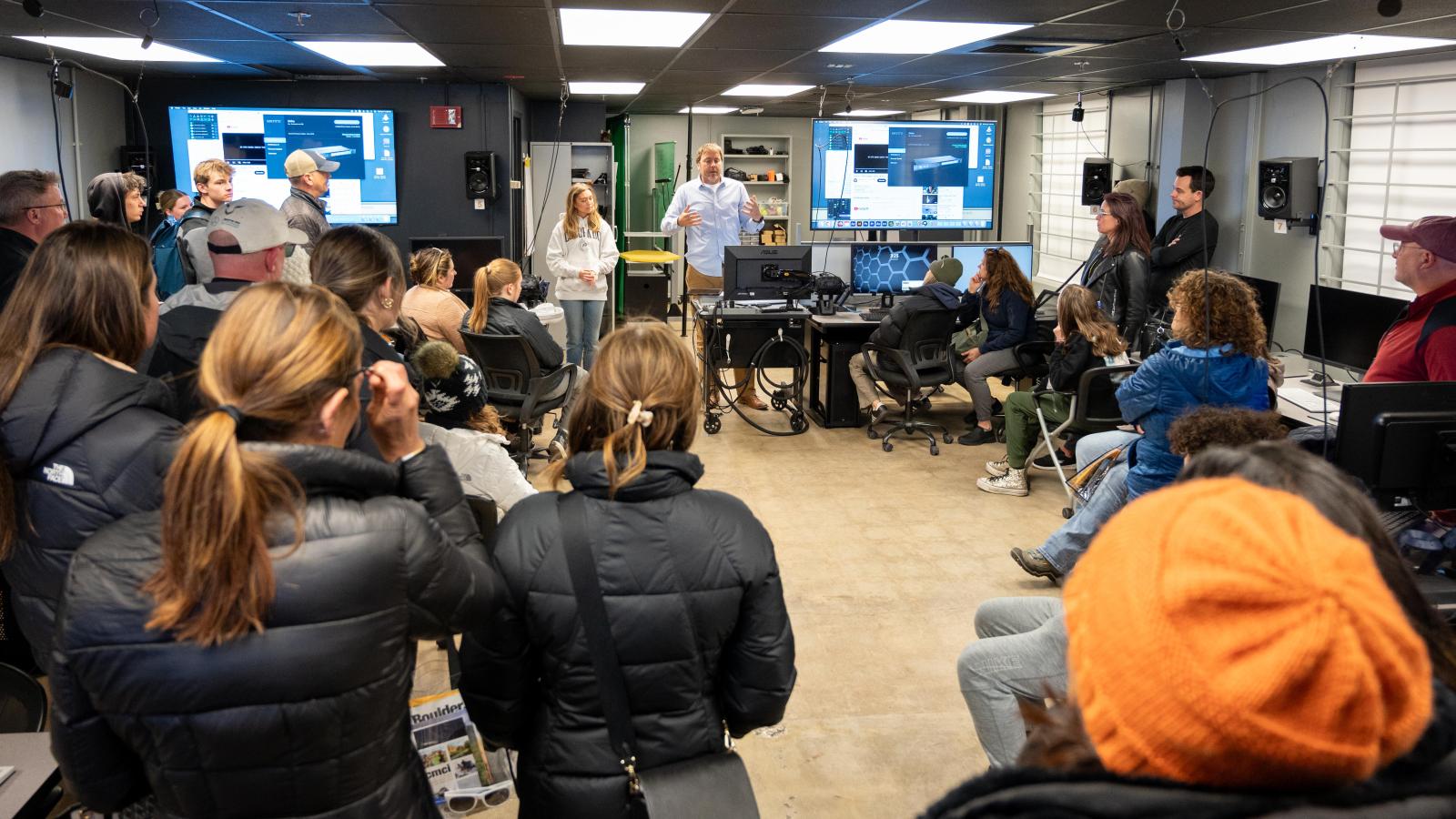 Students and parents watch a virtual reality demonstration in a class.