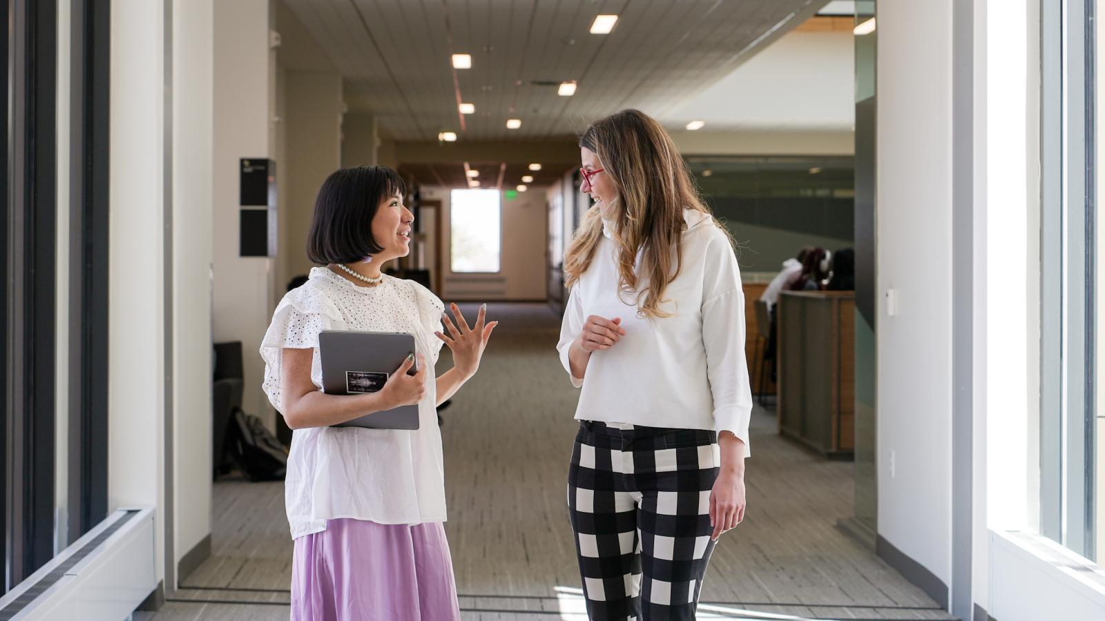 Two women walk down a hallway together.