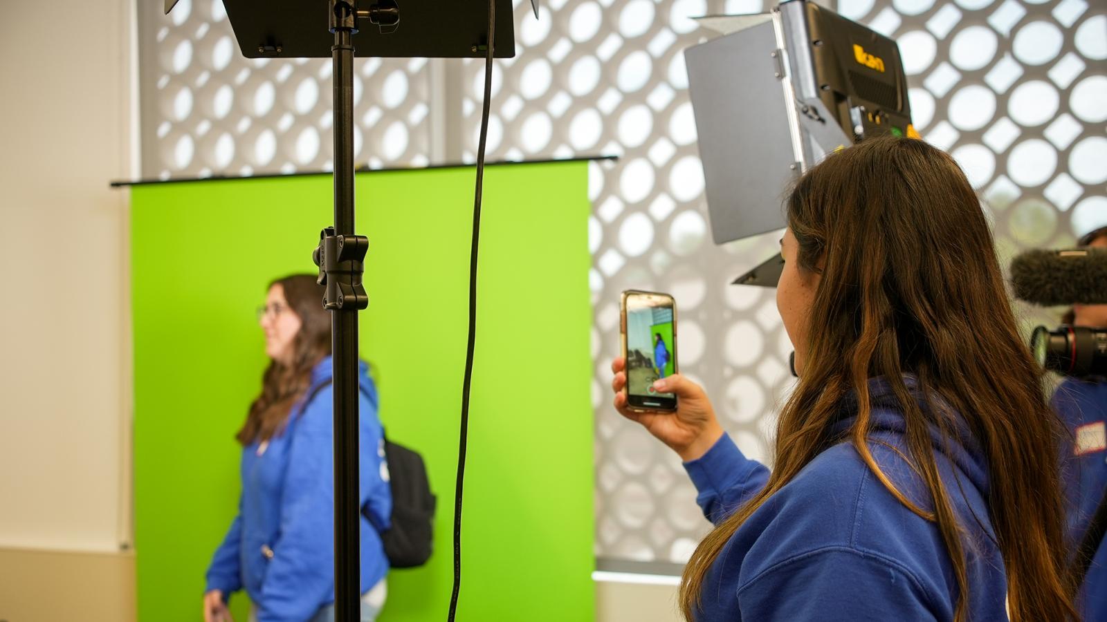 student photographing a colleague in front of a green screen
