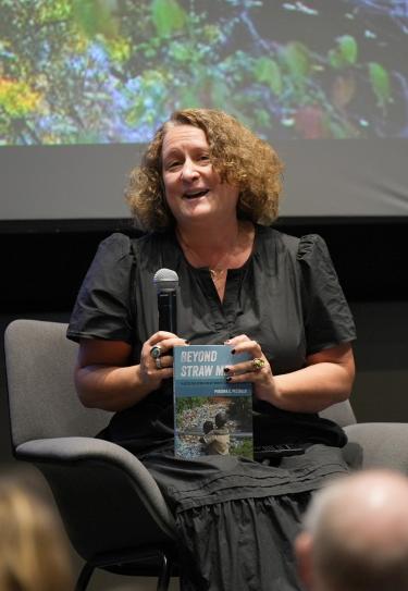 Phaedra Pezzullo answers a question while holding a copy of her book on a stage.