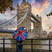A tourist in front of London's Tower Bridge, with a Union Jack umbrella.