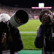 Two students take photos of the crowd during a home football game. 