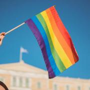 a person holds a Pride flag against a blue sky