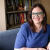 A female professor sits in her office. A bookshelf with books and personal mementoes is in the background.