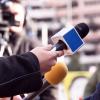 A reporter holds her microphone up to a source as a cameraman takes in the scene in the background.