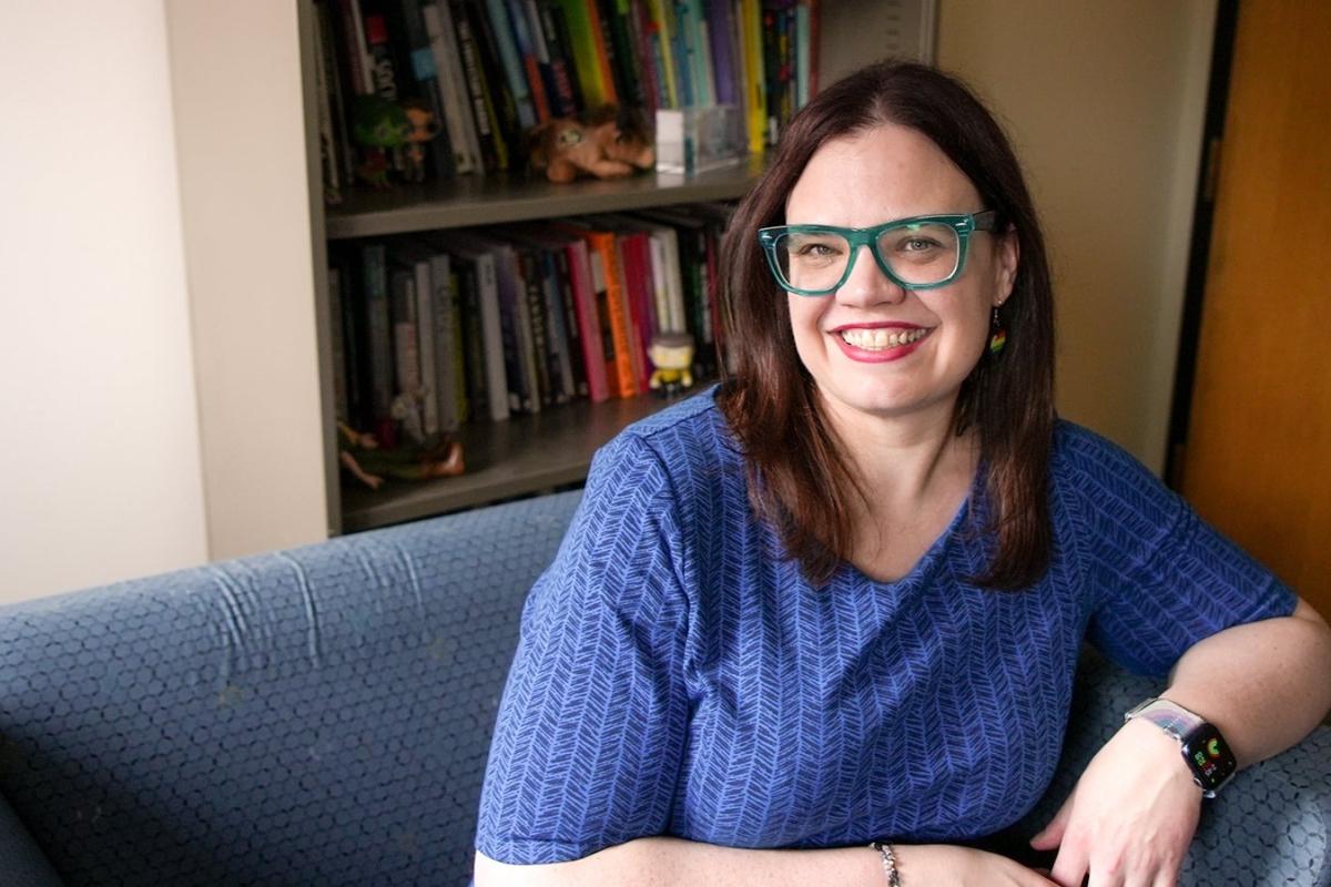A female professor sits in her office. A bookshelf with books and personal mementoes is in the background.