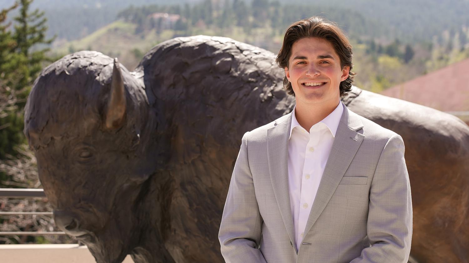 Andrew Johnson poses alongside the buffalo statue on the roof of the CASE building. The Flatirons are visible in the background.