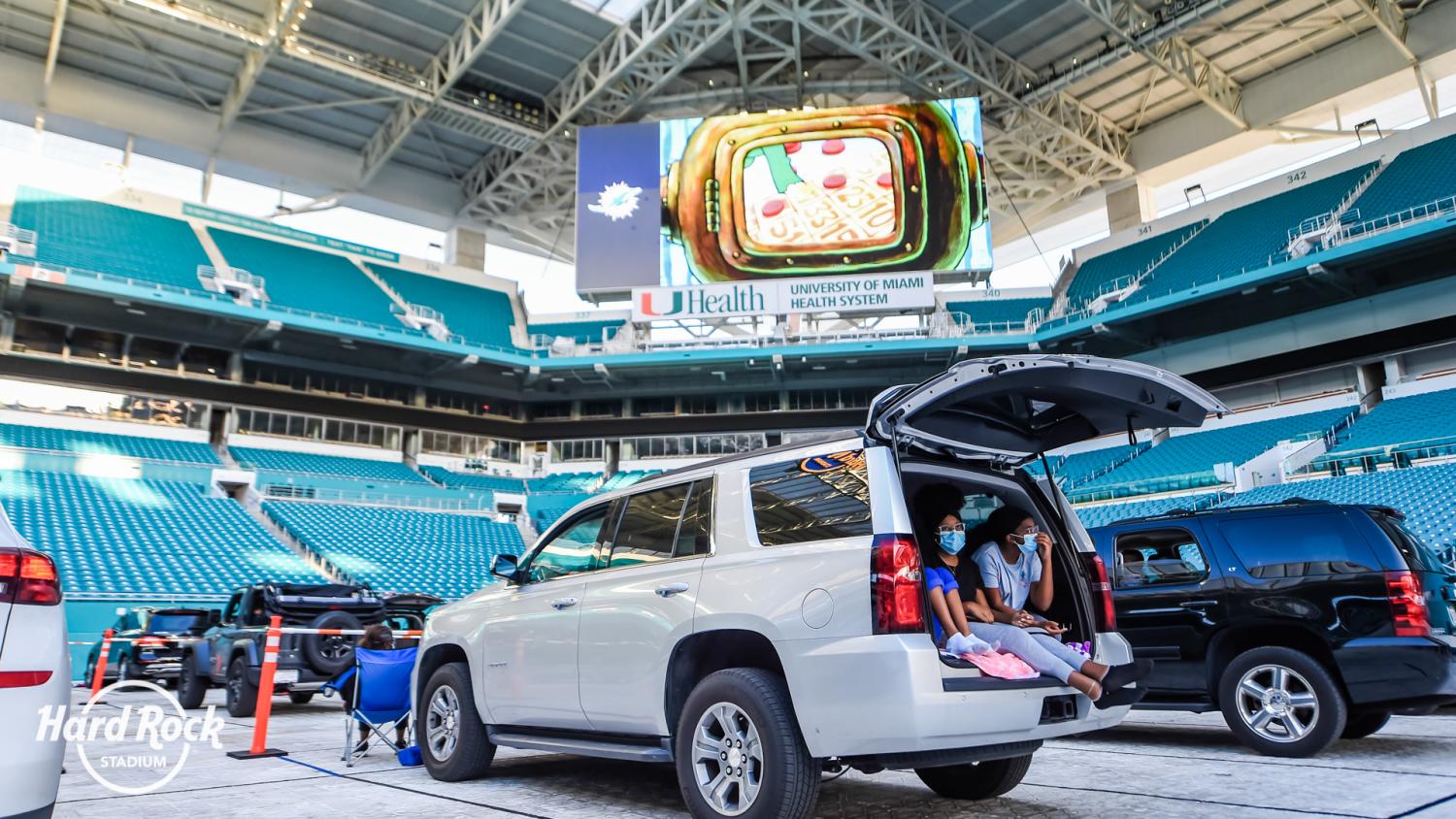 People sitting in a car inside of Hard Rock Stadium with masks on for a drive-in movie.