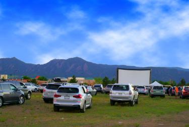 Cars parked for a drive-in theater with Flatirons in the background. 