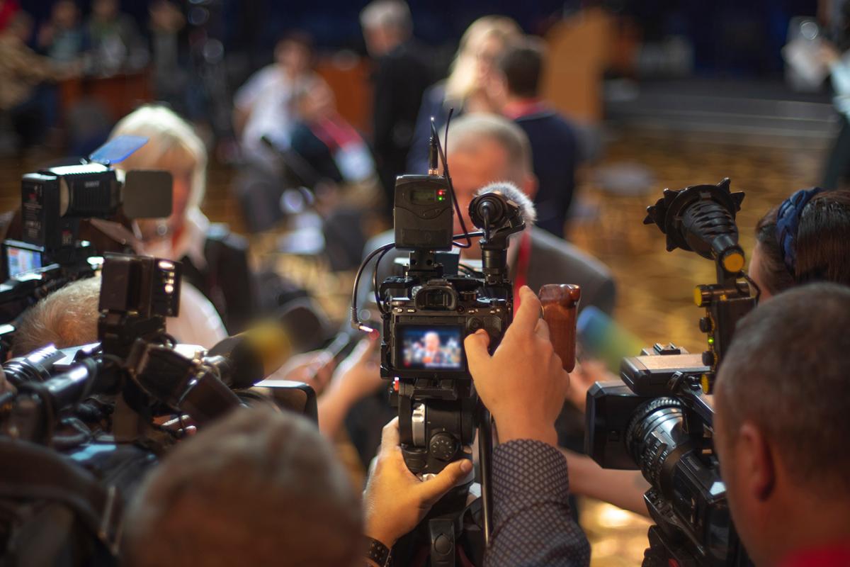 Journalists hold up microphones and recorders as a newsmaker speaks.