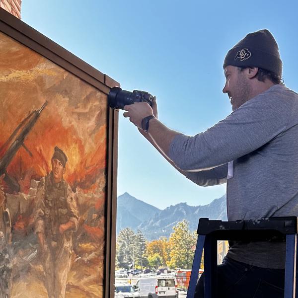 A man on a ladder takes a photo of a painting.
