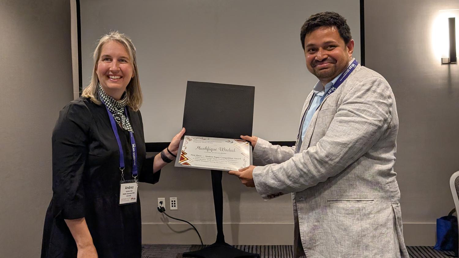 A PhD student accepts an award at a conference.