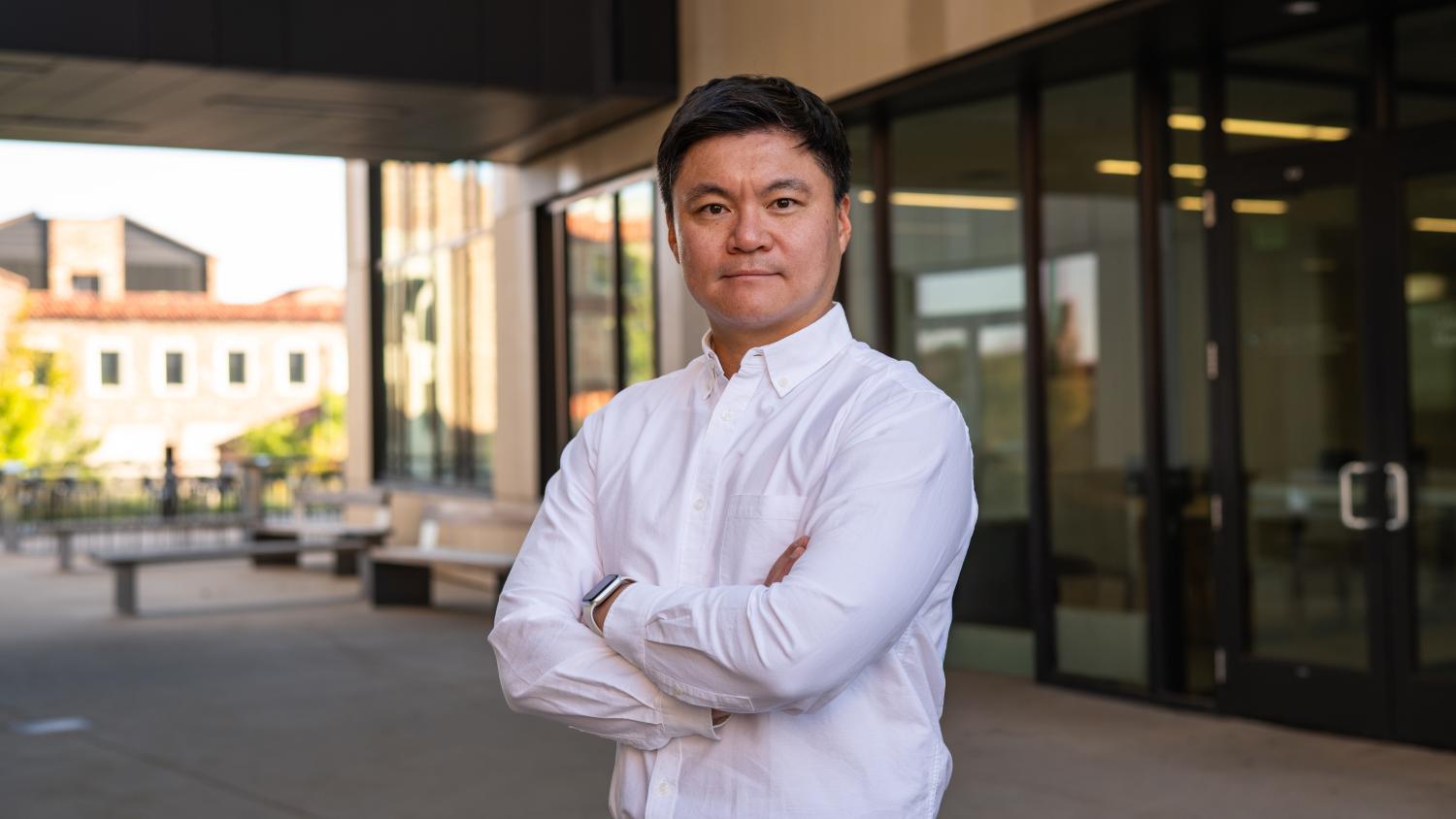 A professor stands with his arms folded in front of an academic building.