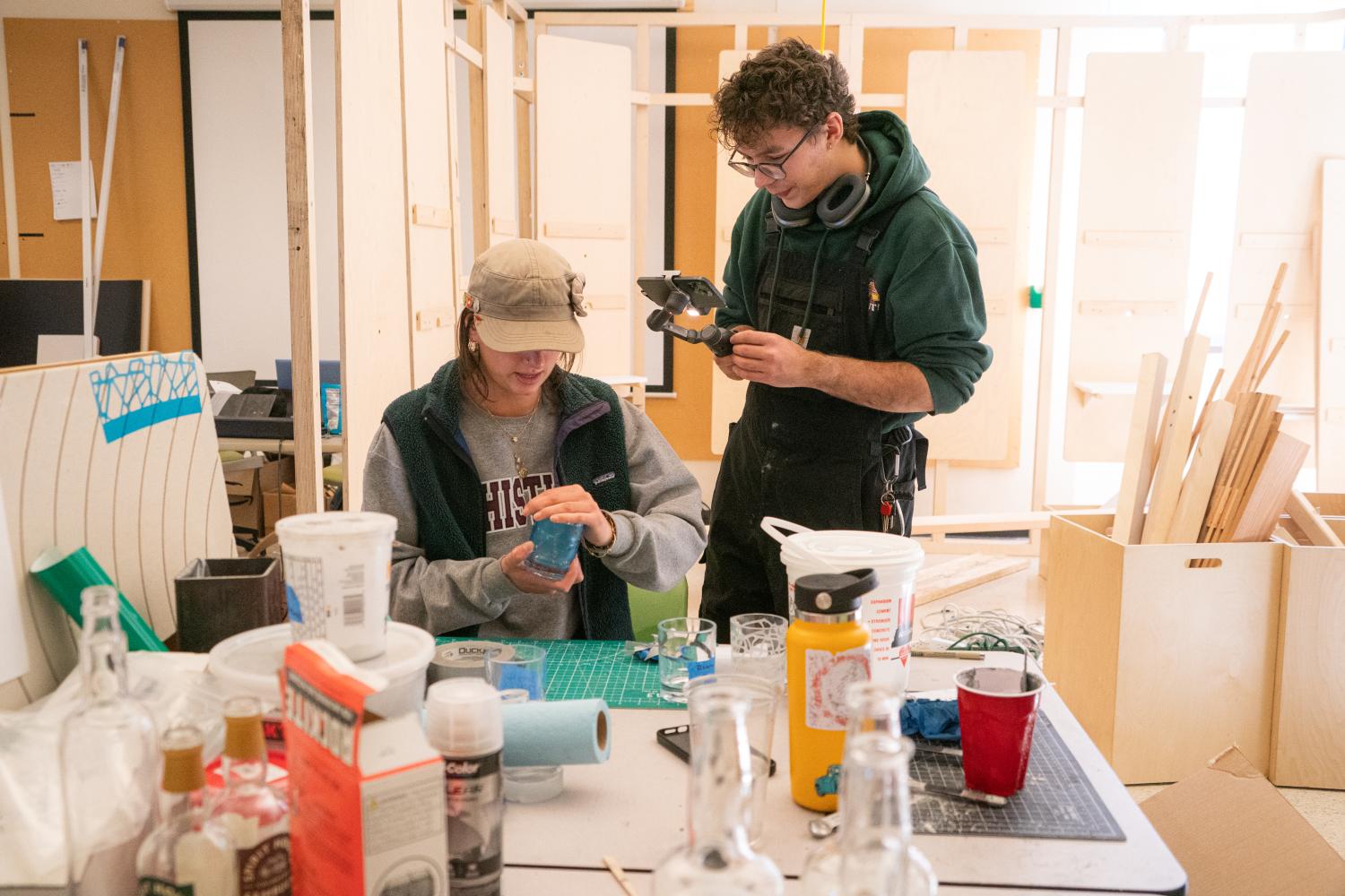 Two students work on their product for the EPOP shop. One student applies a decal to a whiskey glass while the other student films the process.