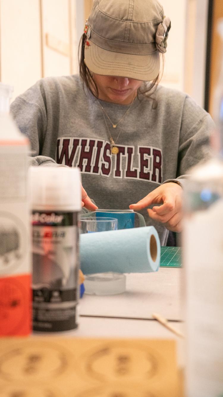 A female student applies a label to a whiskey glass in a lab.
