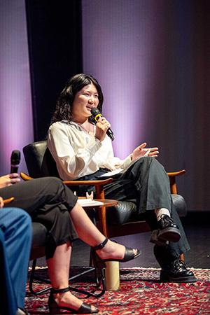A student onstage at a panel event. She's answering a question and speaking into a microphone.