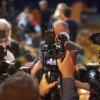 A media scrum of reporters holds up cameras and recorders to capture a newsmaker in the background.