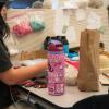 A student works at a table, her water bottle is covered in EPOD stickers