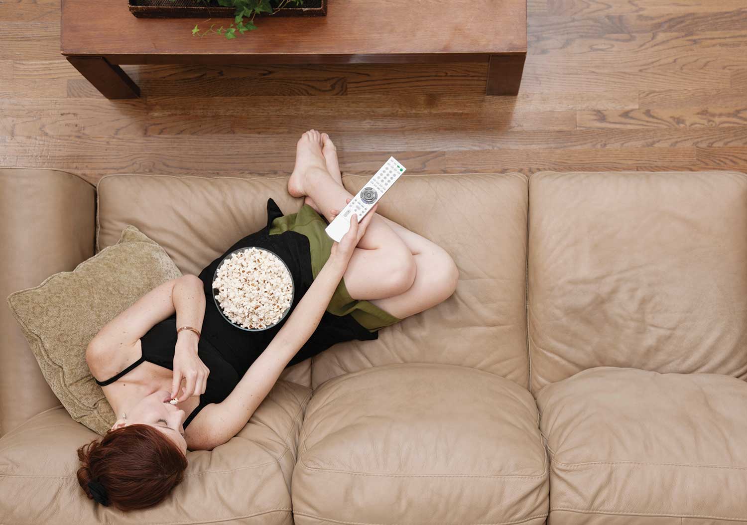 woman on couch eating popcorn holding remote