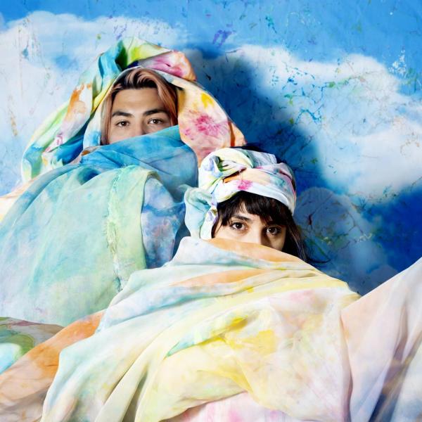 artists Alejandra Abad and Román Anaya sit in the colorful art flags they created
