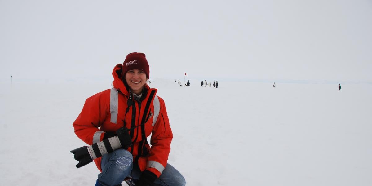 Cassandra Brooks kneeling on an icy terrain with a large camera in hand.